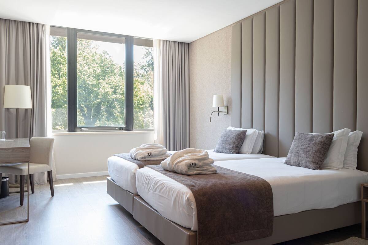 Una habitación de hotel con una cama grande, dos mesitas de noche, un escritorio y una silla.
