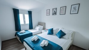 A hotel room with two beds, a window with curtains, and three framed pictures on the wall.