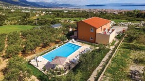 A villa with a swimming pool, surrounded by greenery and a view of the sea and mountains.