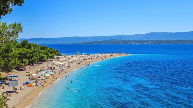A beach with clear blue waters, a sandy shore, and a line of trees.