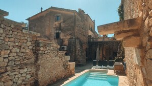 Zona de piscina con muros de piedra y un edificio al fondo.
