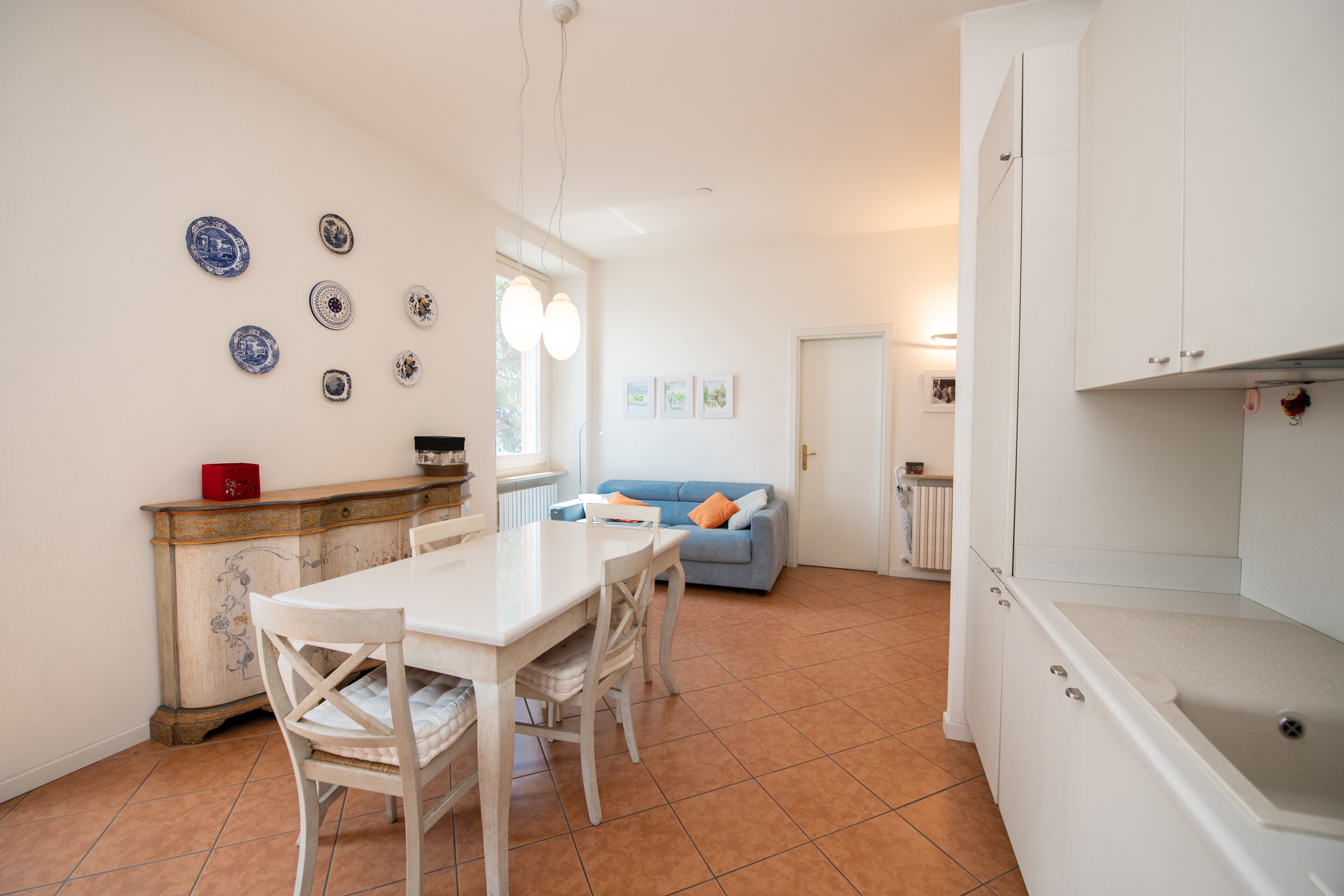 A kitchen with a dining table, chairs, a white cabinet, and a blue sofa in the background.