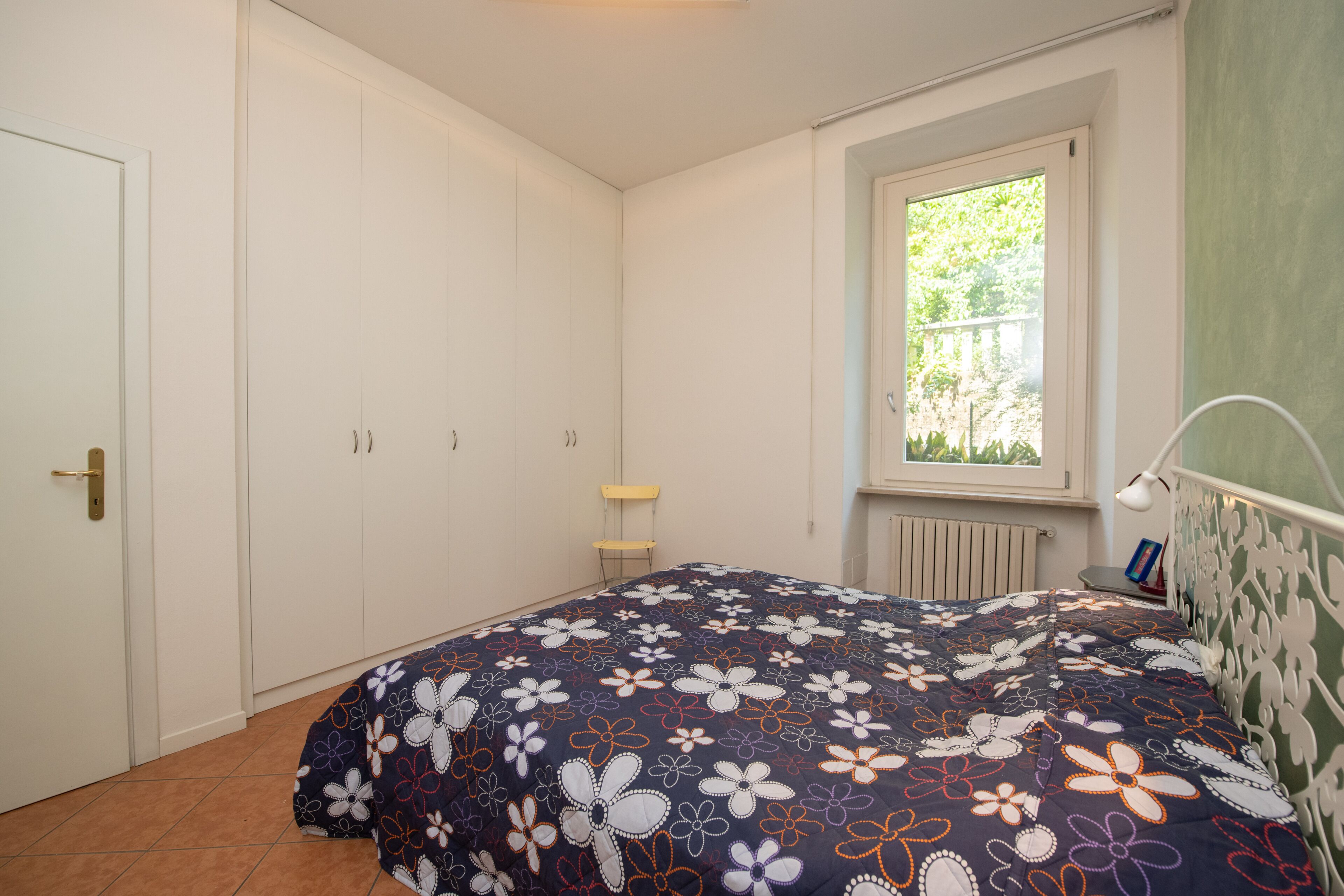 A bedroom with a bed, a window, a radiator, and a door.