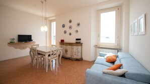Een woonkamer met een blauwe bank, een eettafel met stoelen, een televisie op een plank en decoratieve borden aan de muur.