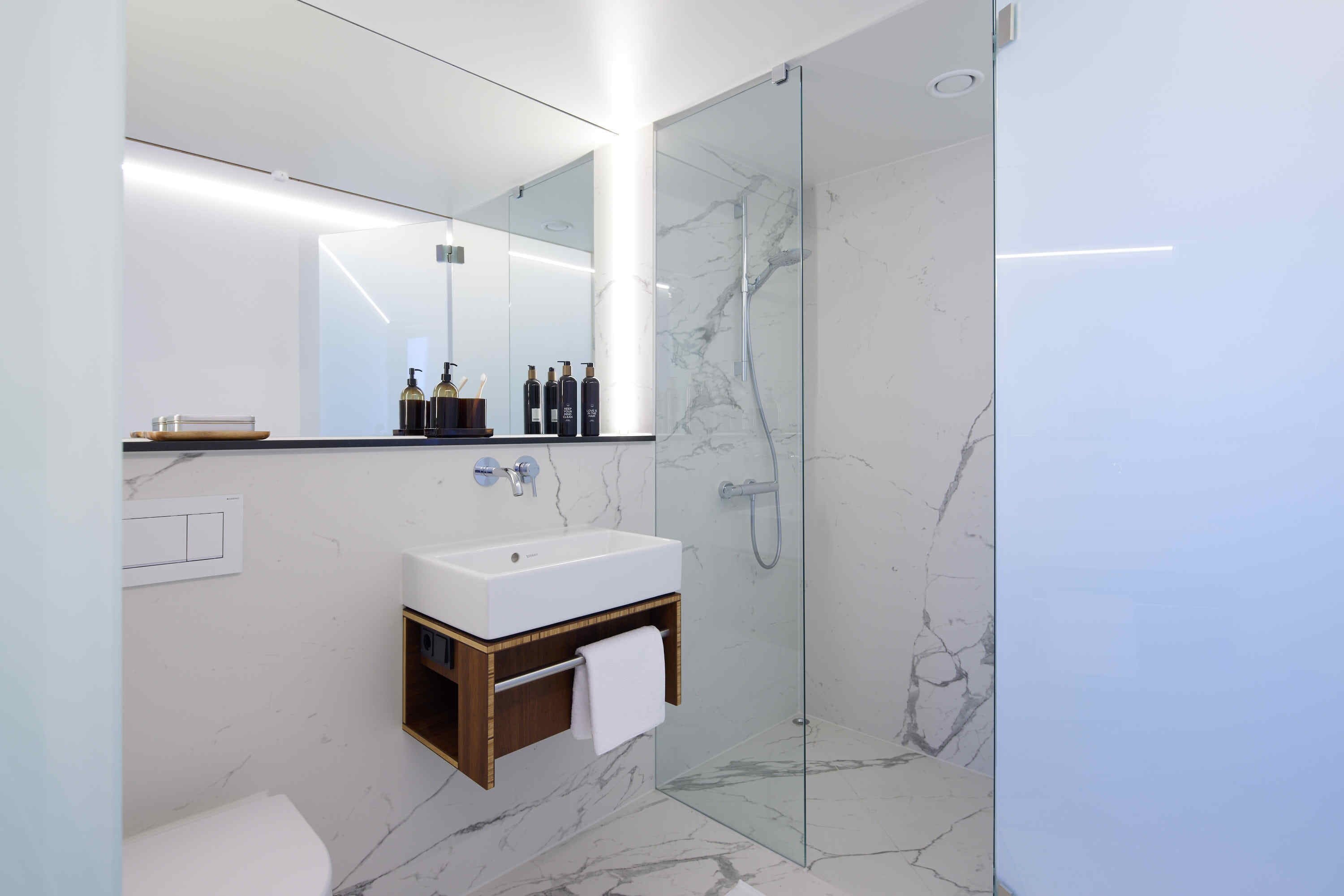 Une salle de bain moderne avec un lavabo blanc, un miroir et une cabine de douche en verre.