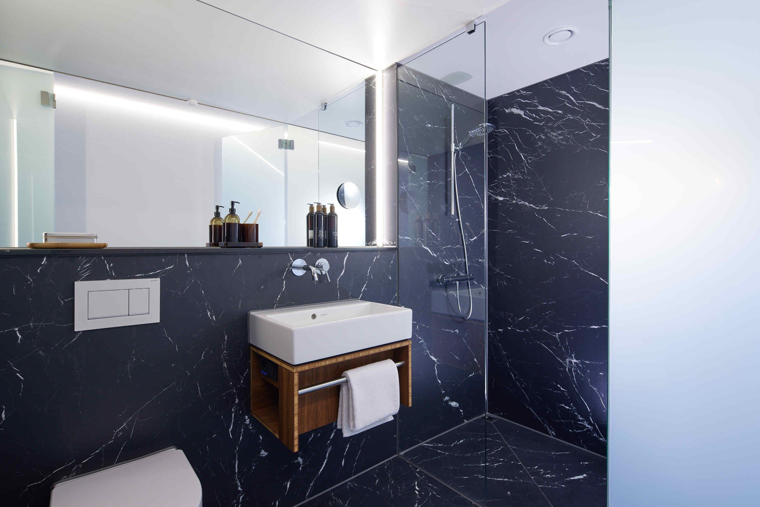 A modern bathroom with a marble sink, a wooden vanity, a glass shower enclosure, and a large mirror.