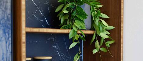 A wooden shelf with a marble backsplash, a potted plant, and two black cylindrical containers.