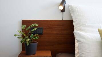 A wooden bedside table with a potted plant, a wall-mounted lamp, and a white pillow.