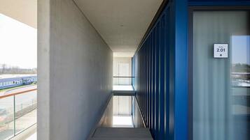 A corridor with a glass railing, a blue wall, and a door labeled "Zimmer 2.01".