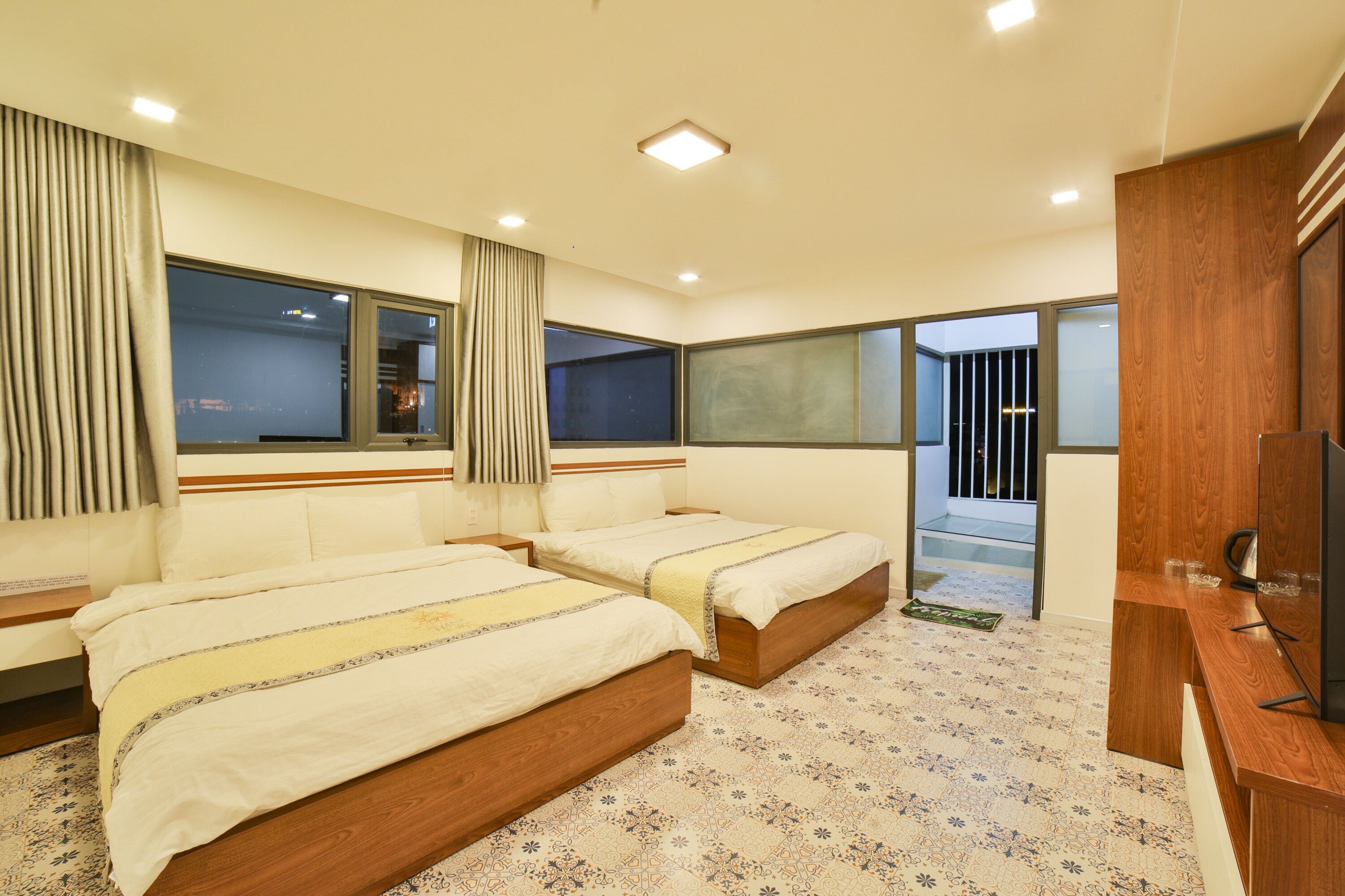A hotel room with two beds, a wooden desk, and a large window.