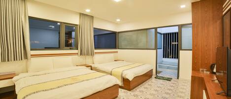 A hotel room with two beds, a wooden desk, and a large window.