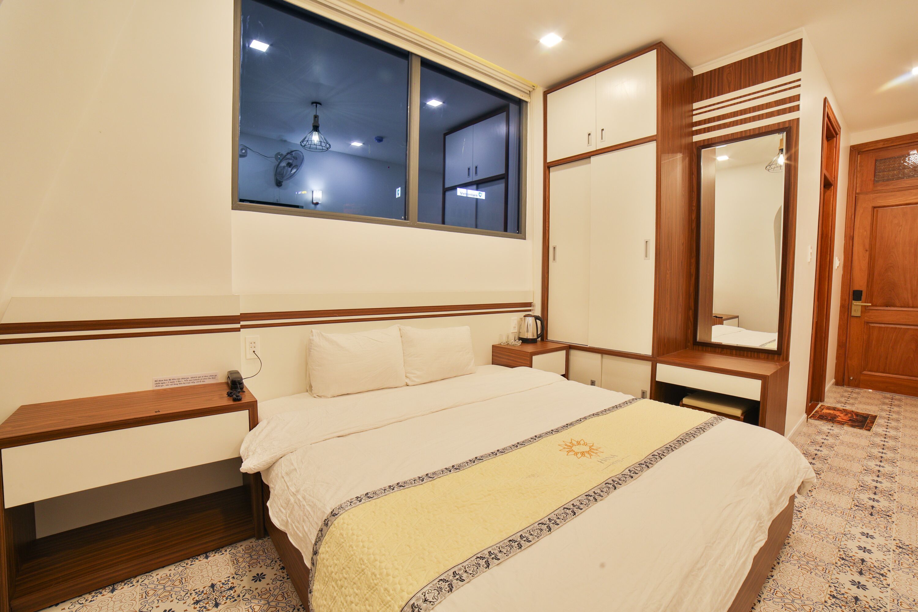A neatly arranged bedroom with a bed, bedside tables, a wardrobe, and a window with a view.
