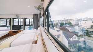 Un dormitorio con un ventanal grande, una cama, un televisor y un ventilador.