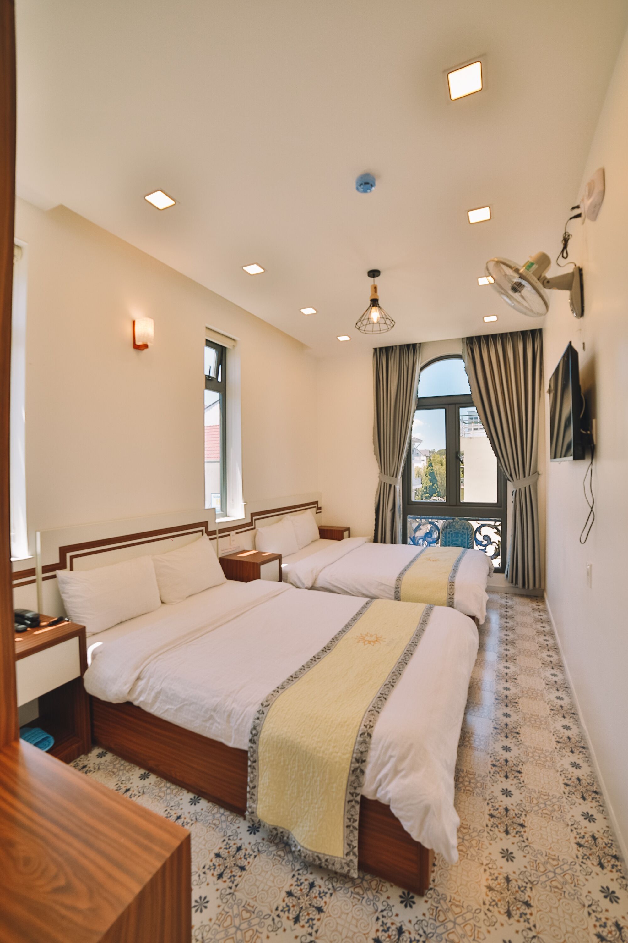 A hotel room with two beds, a small table, a TV, and a balcony with a view.