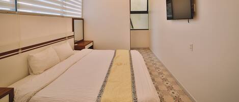 Un dormitorio con cama, mesita de noche, televisor de pared, ventilador de techo y persianas.