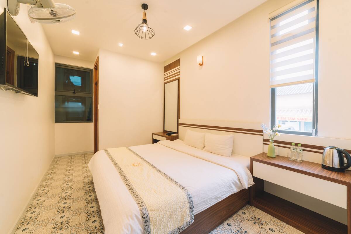 A hotel room with a bed, bedside table, and a window with blinds.