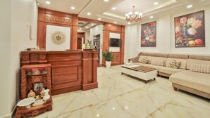 Un hall de hotel con mostrador de recepción, un conjunto de sofás, una araña y obras de arte en las paredes.
