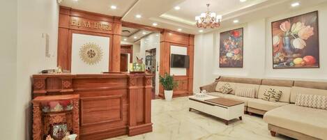 A hotel lobby with a reception desk, a sofa set, a chandelier, and artwork on the walls.