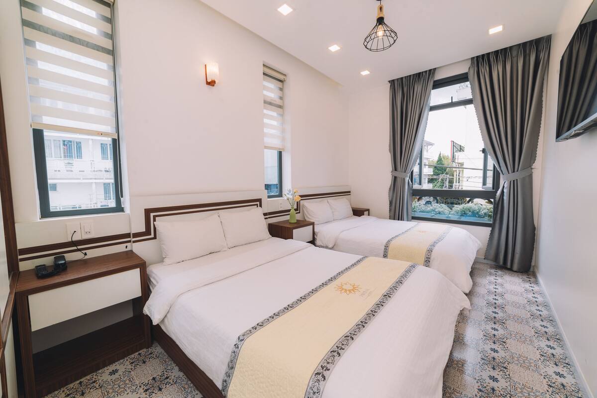 A hotel room with two beds, a nightstand, a small table, and a window with curtains.