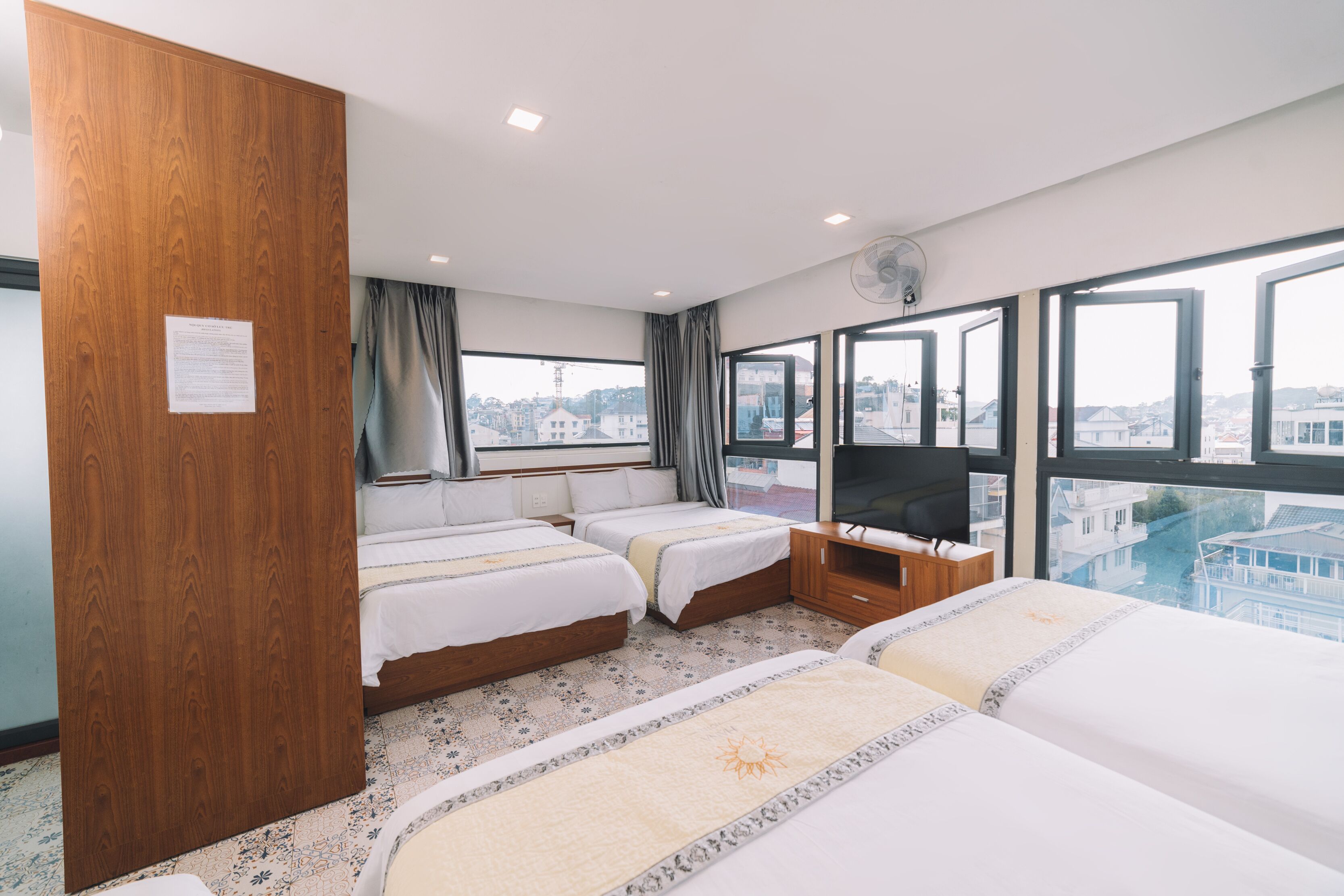 A hotel room with two beds, a TV, and a large window offering a city view.