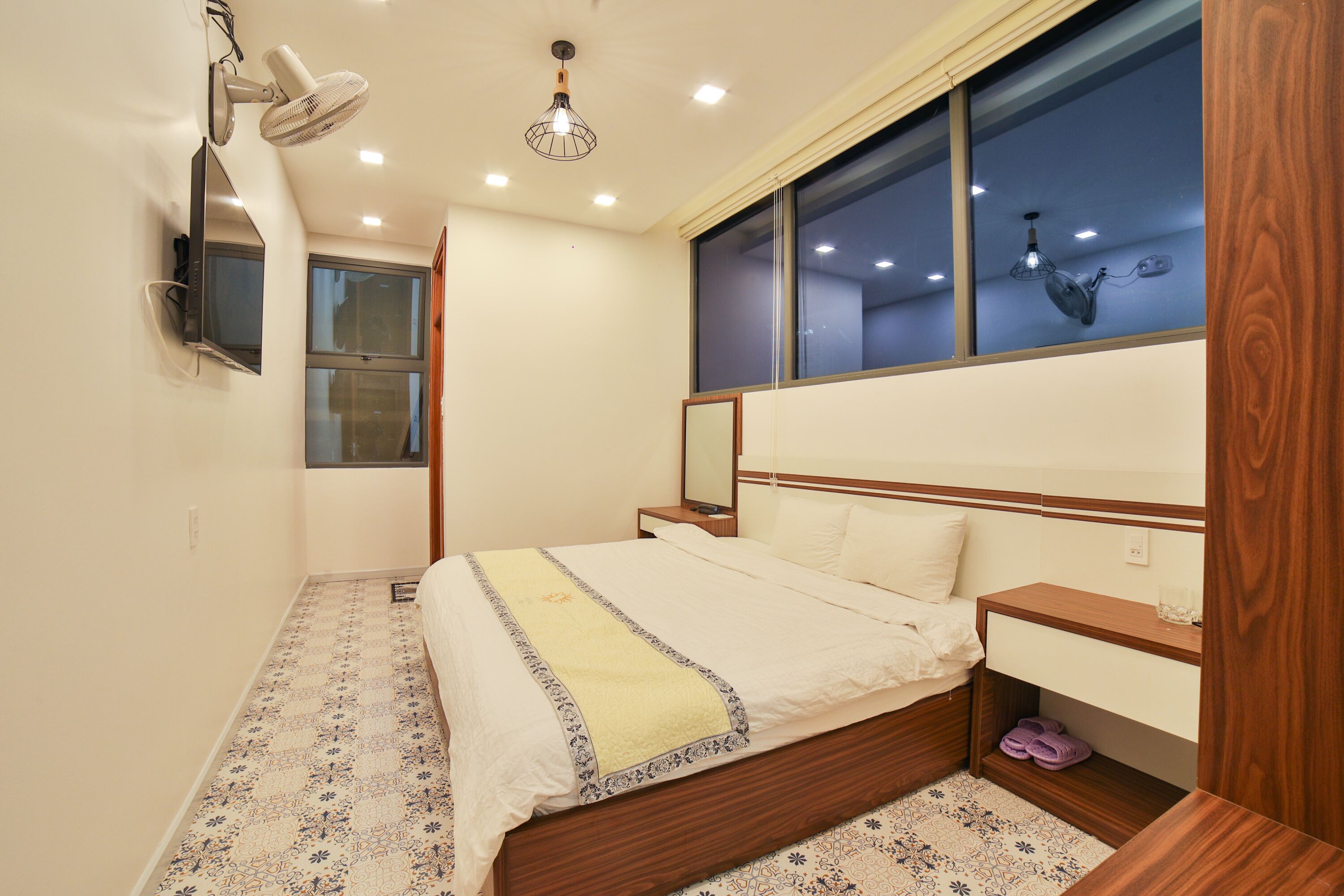 A bedroom with a bed, bedside table, nightstand, and a window with a view.