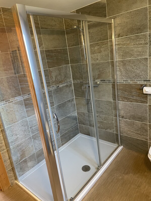 A walk-in shower with a glass door, tiled walls, and a wooden floor.