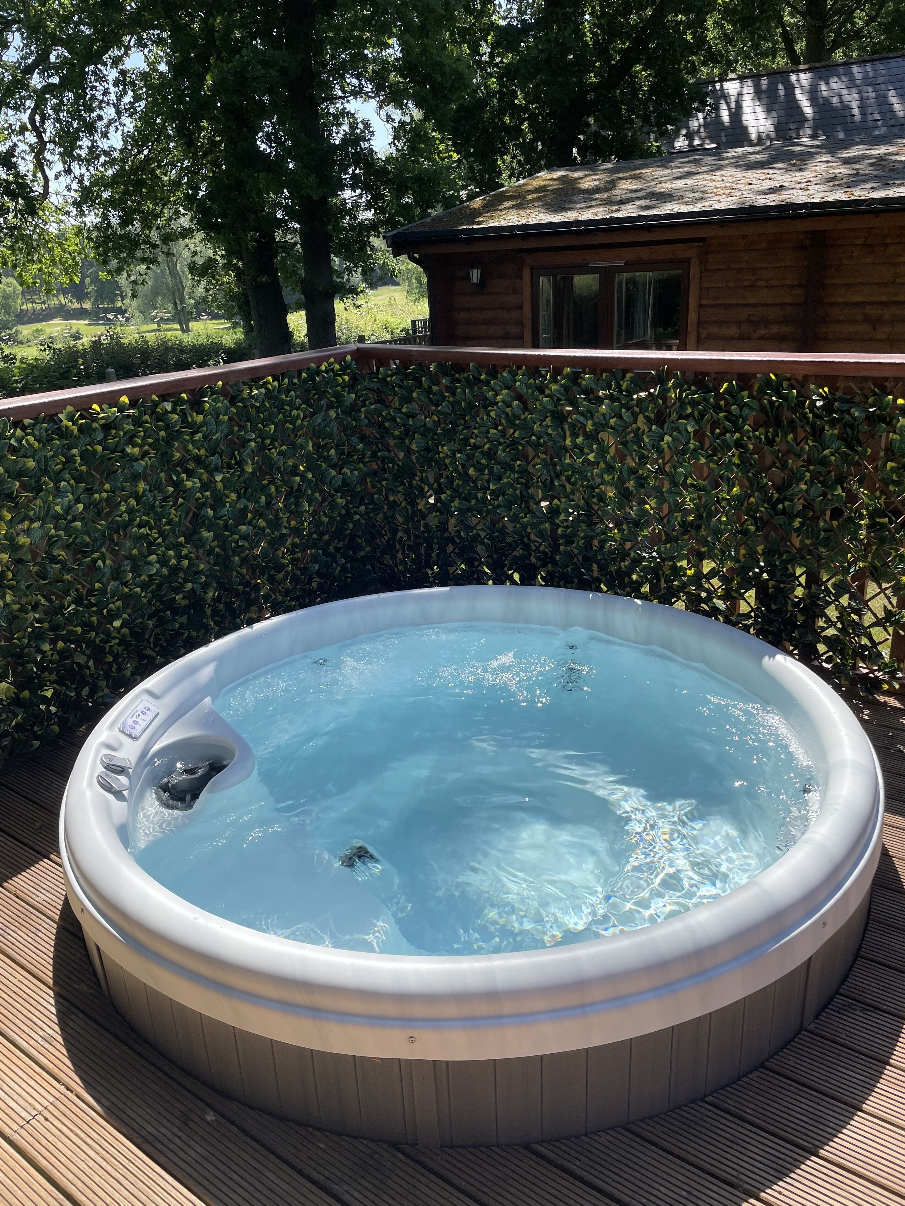 Un jacuzzi en una terraza de madera, con una cabaña de madera al fondo.
