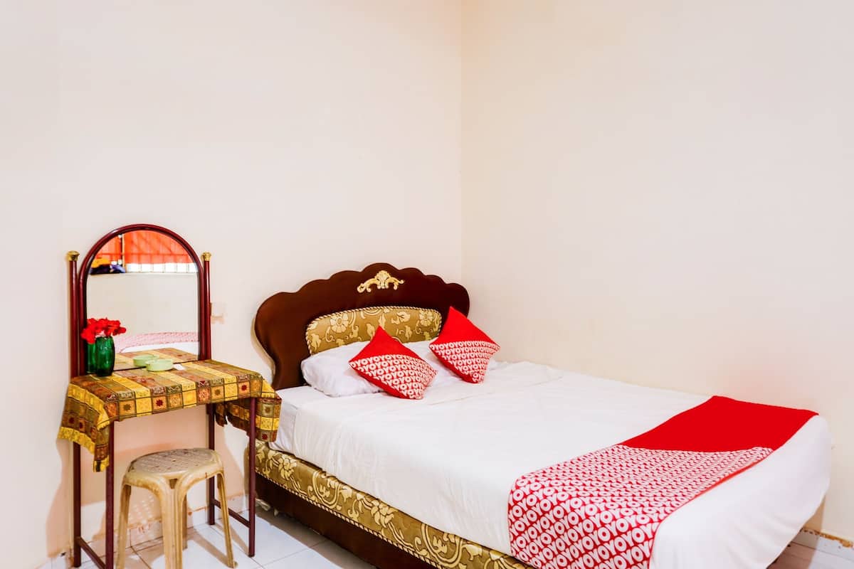 Un dormitorio ordenado con cama, mesita de noche, espejo y taburete.