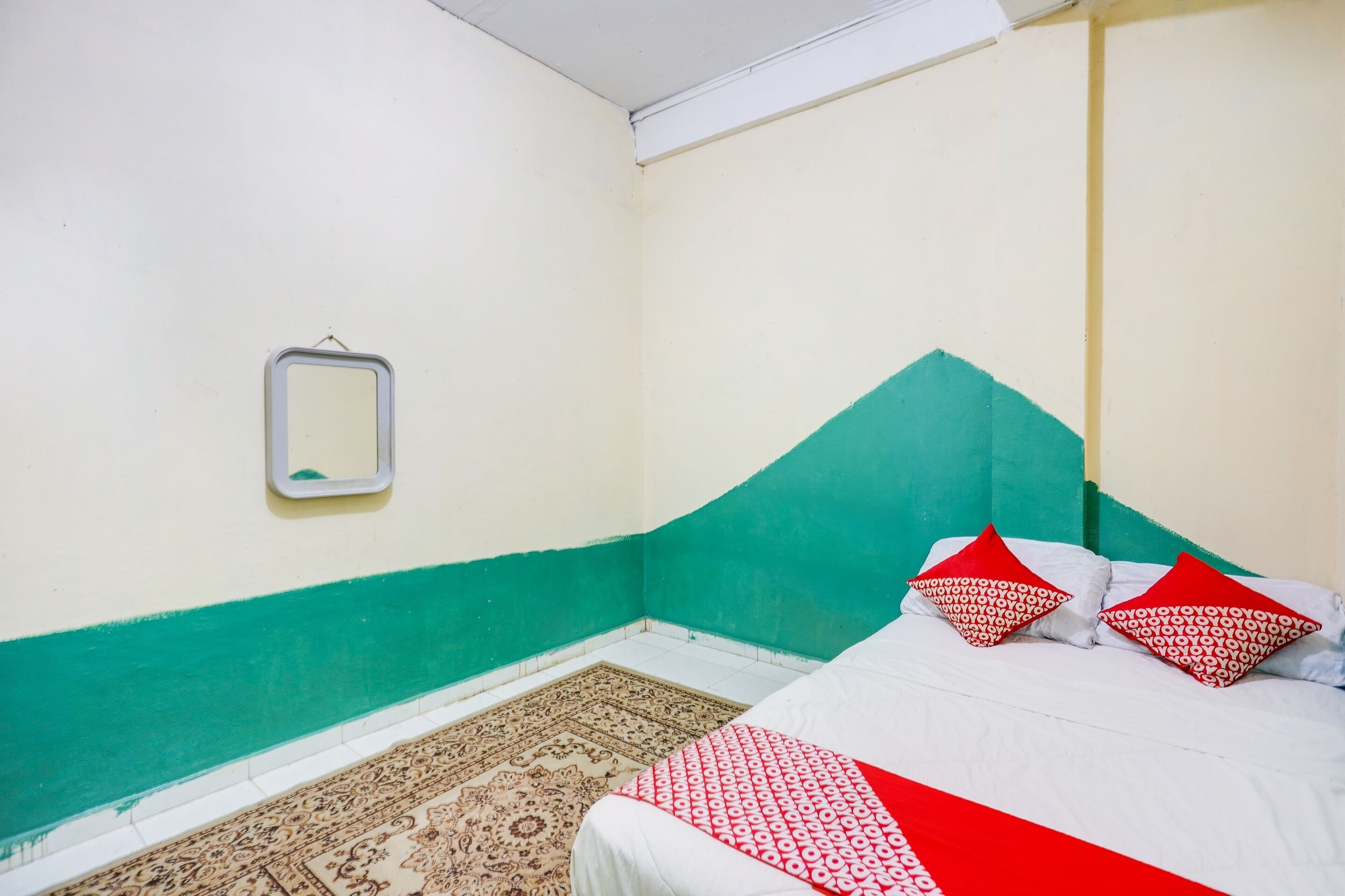A bedroom with a bed, a small mirror, and a patterned rug.