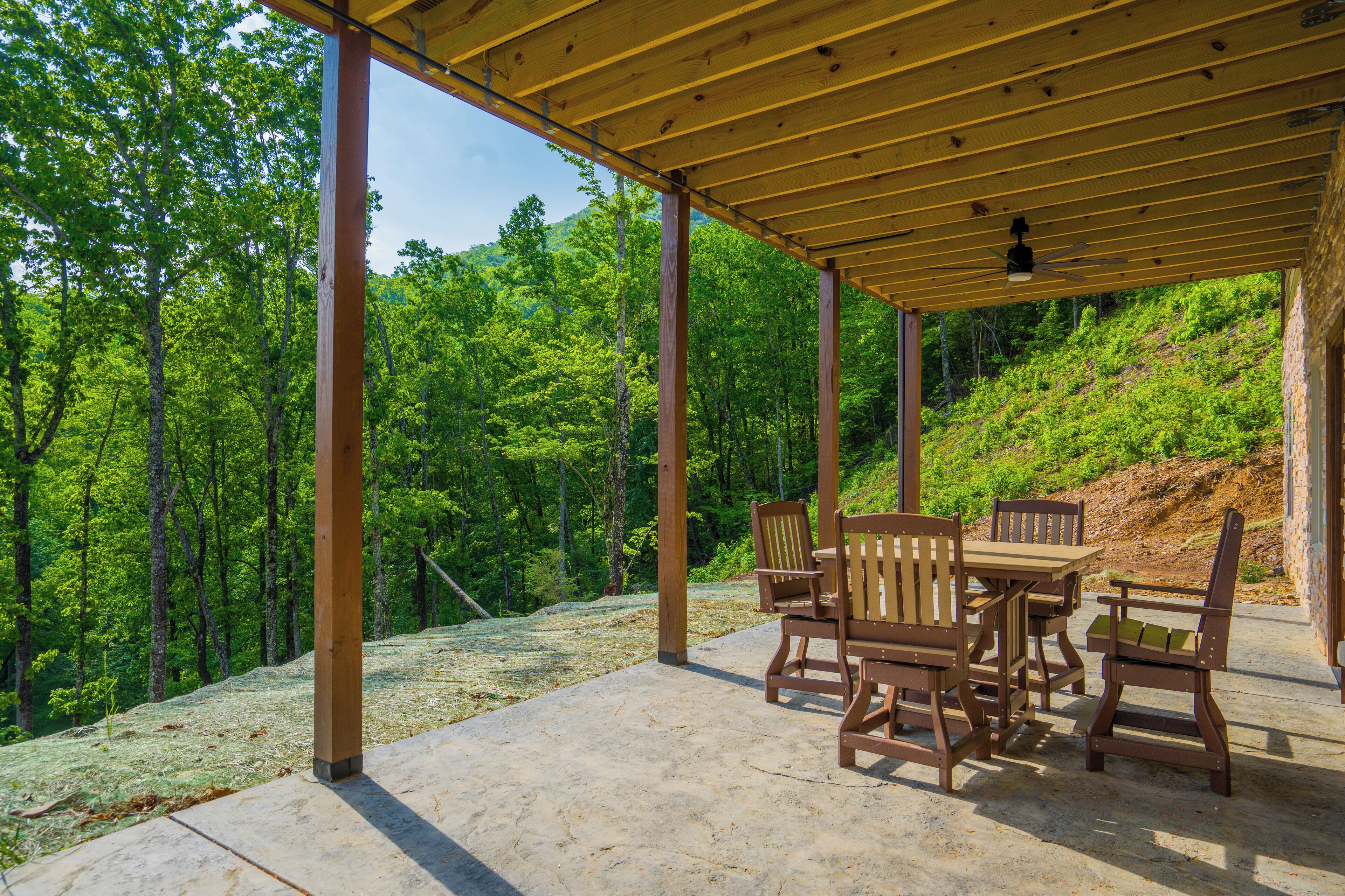 Zona relax all'aperto, riparata, con mobili in legno e vista su un pendio boscoso.
