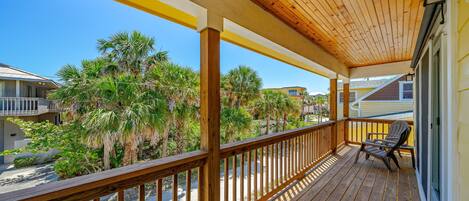 Una terraza de madera con barandilla, con vista a una playa con palmeras y casas.