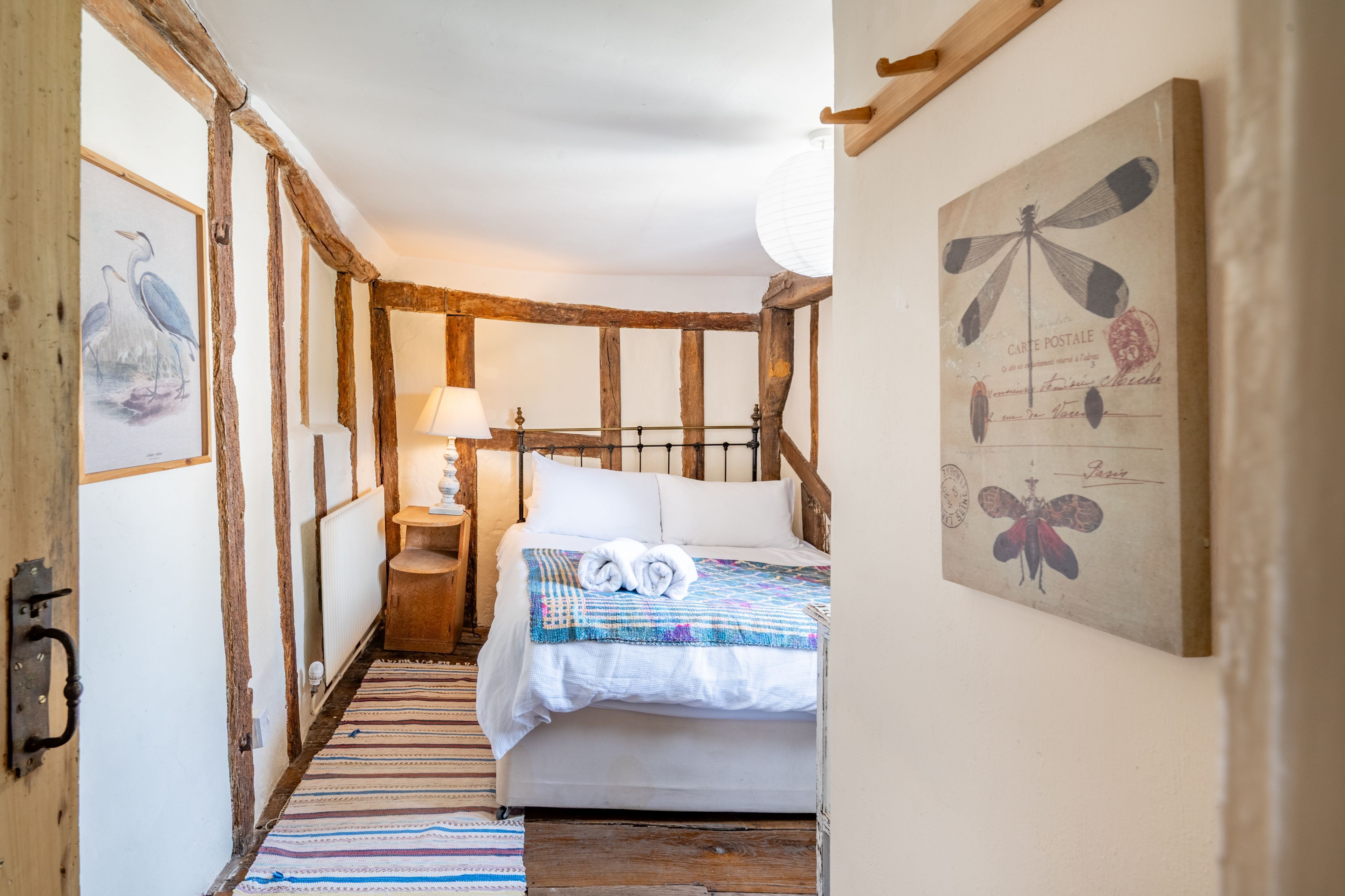 A narrow room with a bed, a lamp, and a framed artwork on the wall.