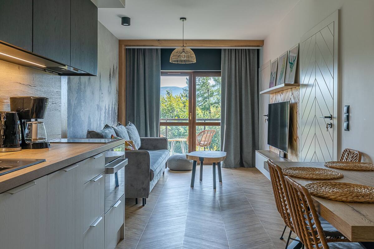 A modern kitchen with a dining area, large windows, and a view of the outdoors.
