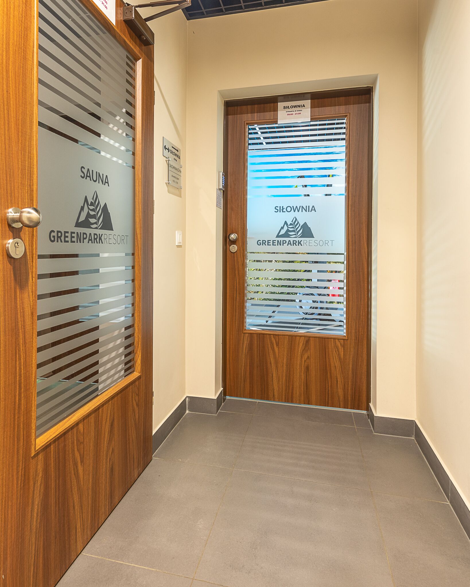A hallway with a wooden door labeled "SAUNA GREENPARKRESORT" and a poster with "SILOWNIA" and "GREENPARKRESORT" text.