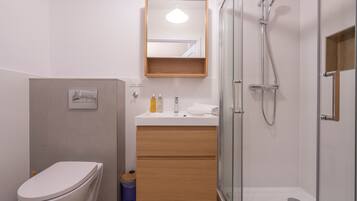 A modern bathroom with a toilet, sink, mirror, and shower.