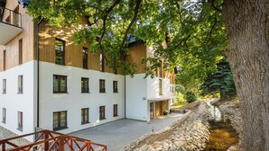 A modern building with a stone-lined water channel, wooden balconies, and a red bridge. - RentPlanet - Green Park Resort (Szklarska Poreba)