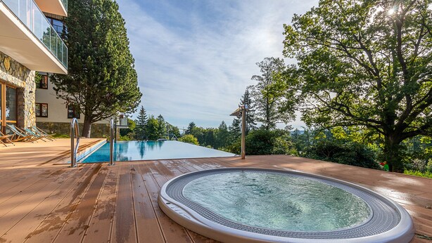 A wooden deck with a hot tub, a swimming pool, and a building with a stone facade. - RentPlanet - Green Park Resort (Szklarska Poreba)