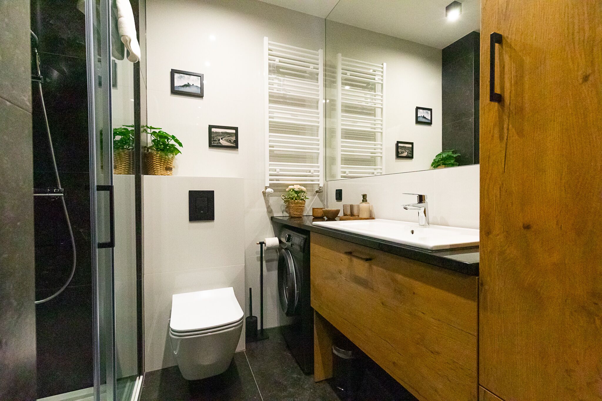 Une salle de bain moderne avec une douche à parois de verre, des toilettes blanches, un meuble-lavabo en bois et un grand miroir.