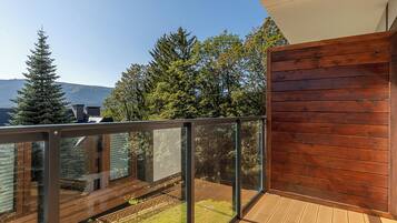 A balcony with a glass railing, wooden deck, and a view of trees and mountains.