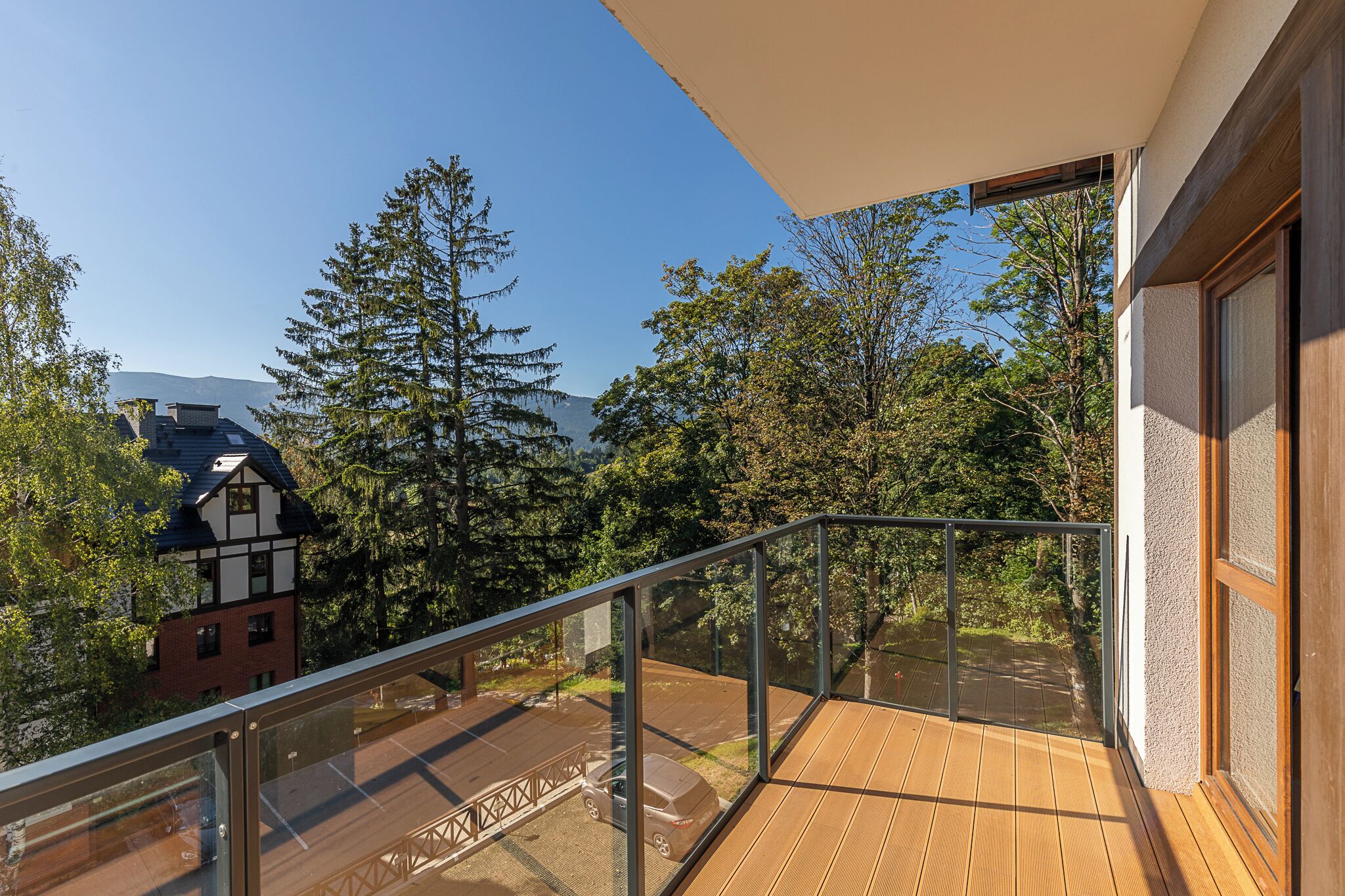 Ein Balkon mit Glasgeländer, der auf einen Parkplatz und Bäume blickt.