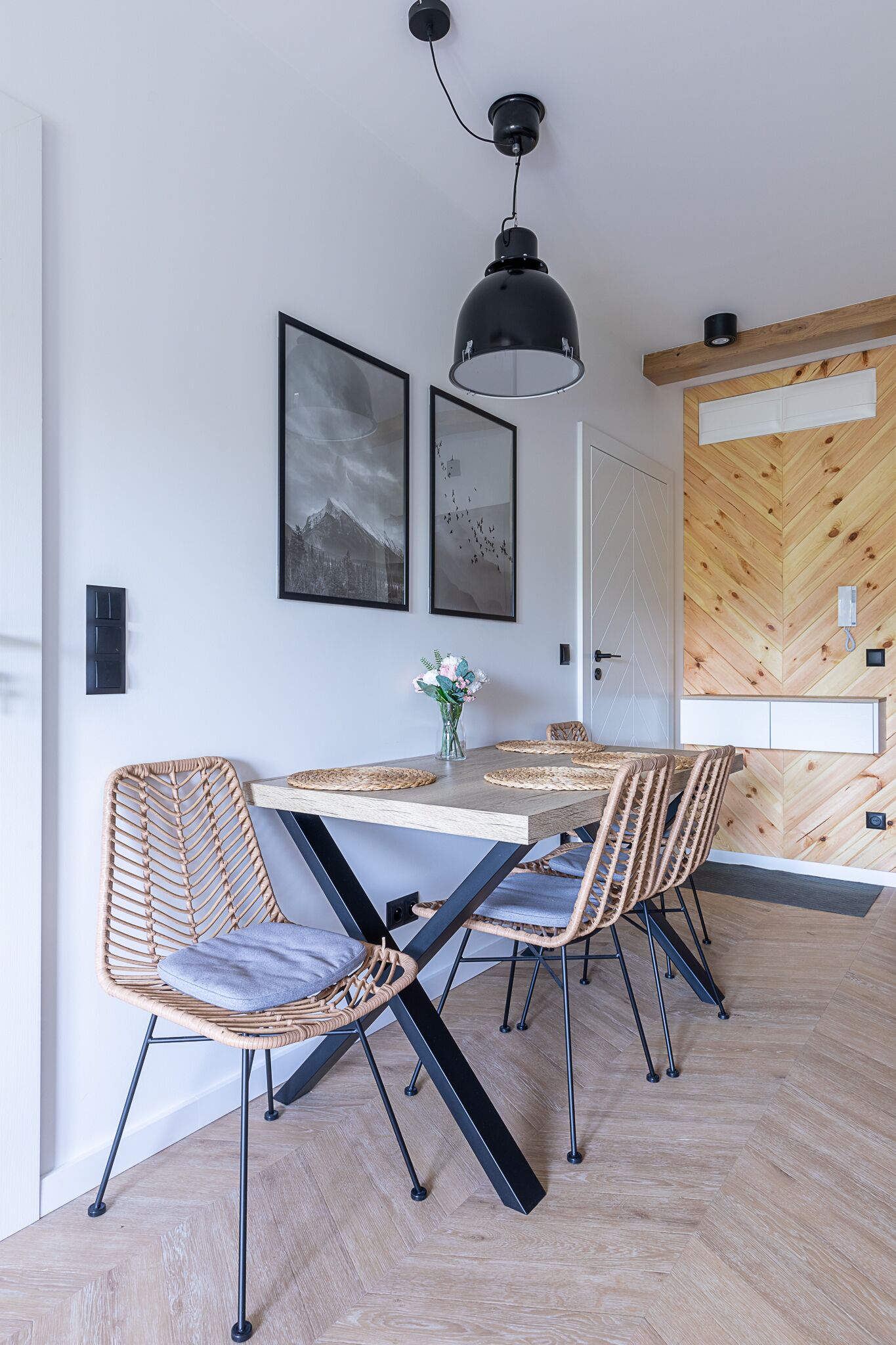 A dining area with a wooden herringbone floor, a table with woven chairs, and two framed pictures on the wall.