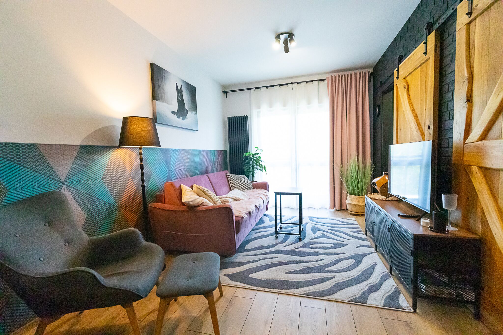 Ein modernes Wohnzimmer mit einer Couch, Sesseln, einem Fernseher und einem gemusterten Teppich.
