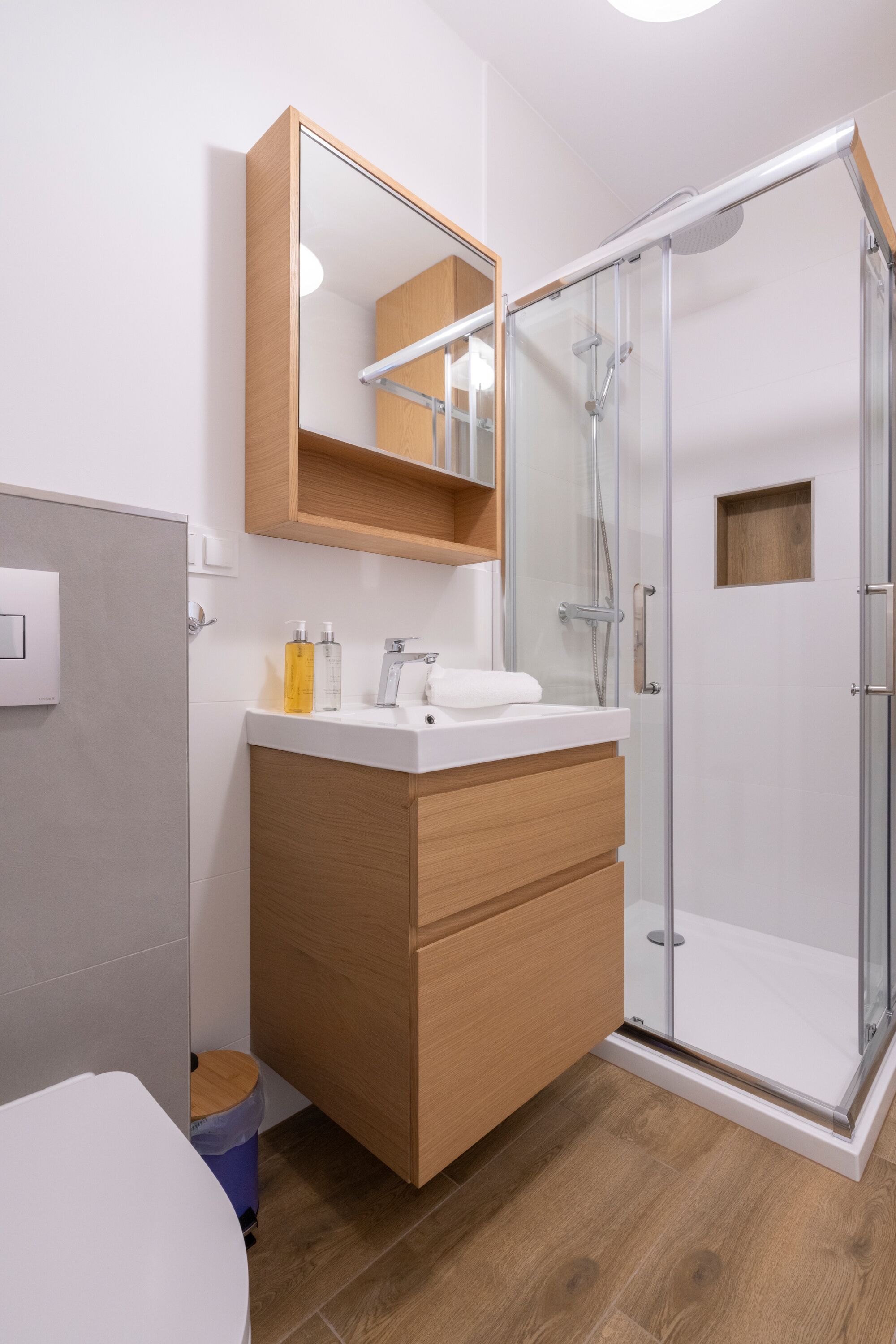 A modern bathroom with a glass-enclosed shower, a wooden vanity with a mirror, and a white sink.