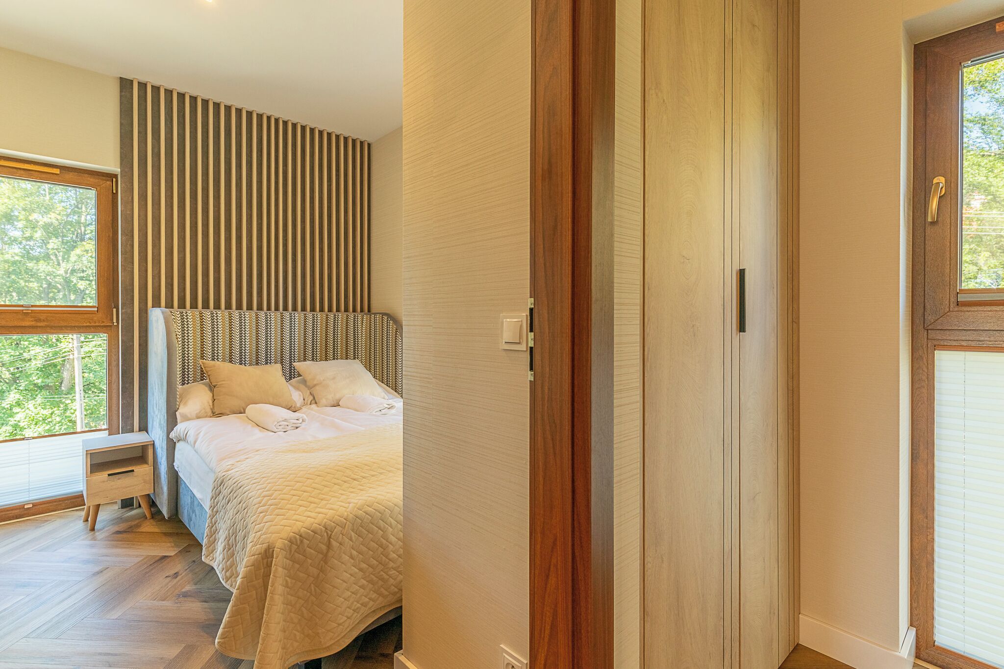 Une chambre à coucher avec un grand lit, une table de chevet, une armoire en bois et une fenêtre avec des stores.