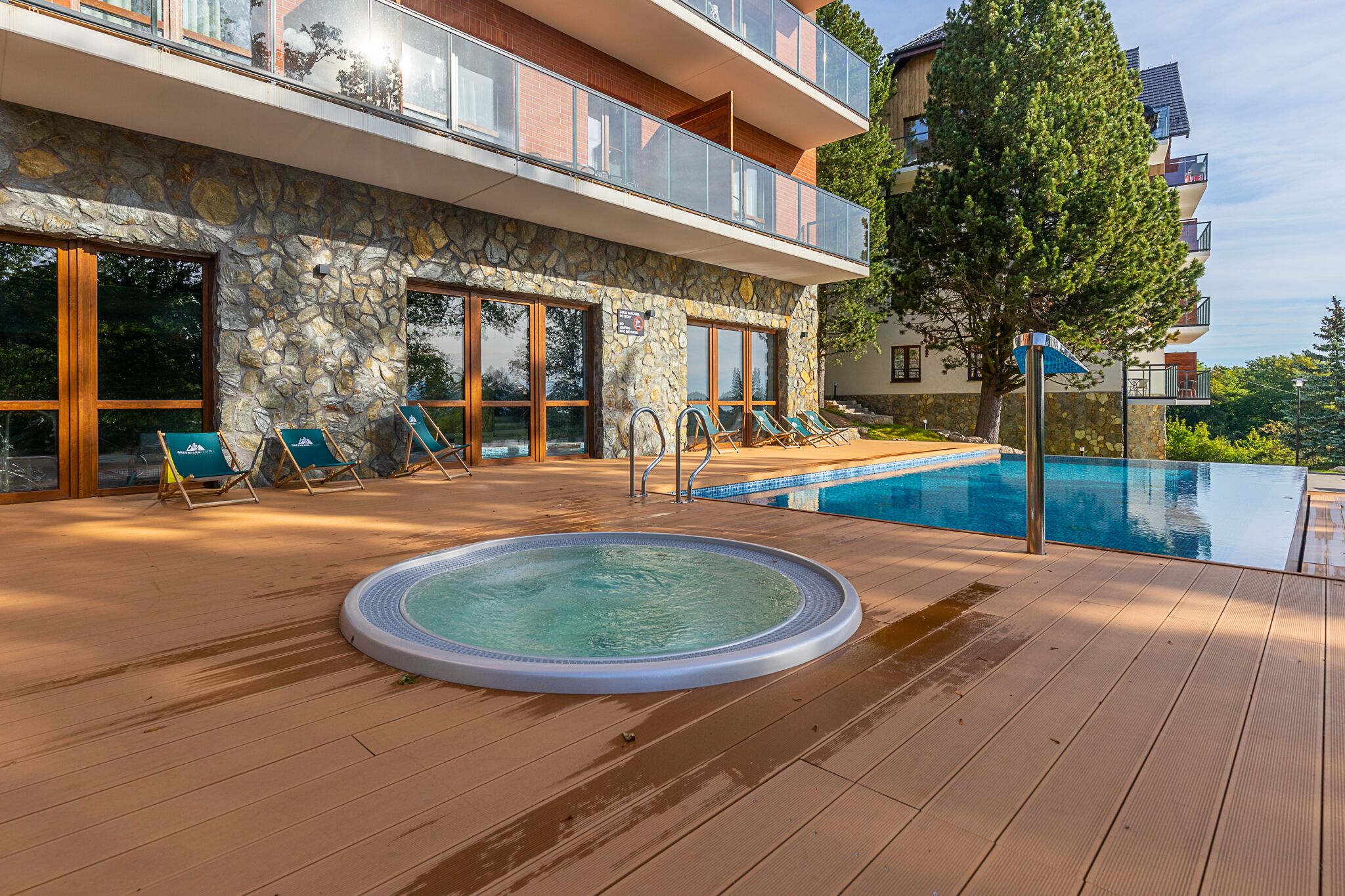 Un espace piscine doté d’un jacuzzi, de chaises longues et d’un bâtiment en pierre avec des balcons.