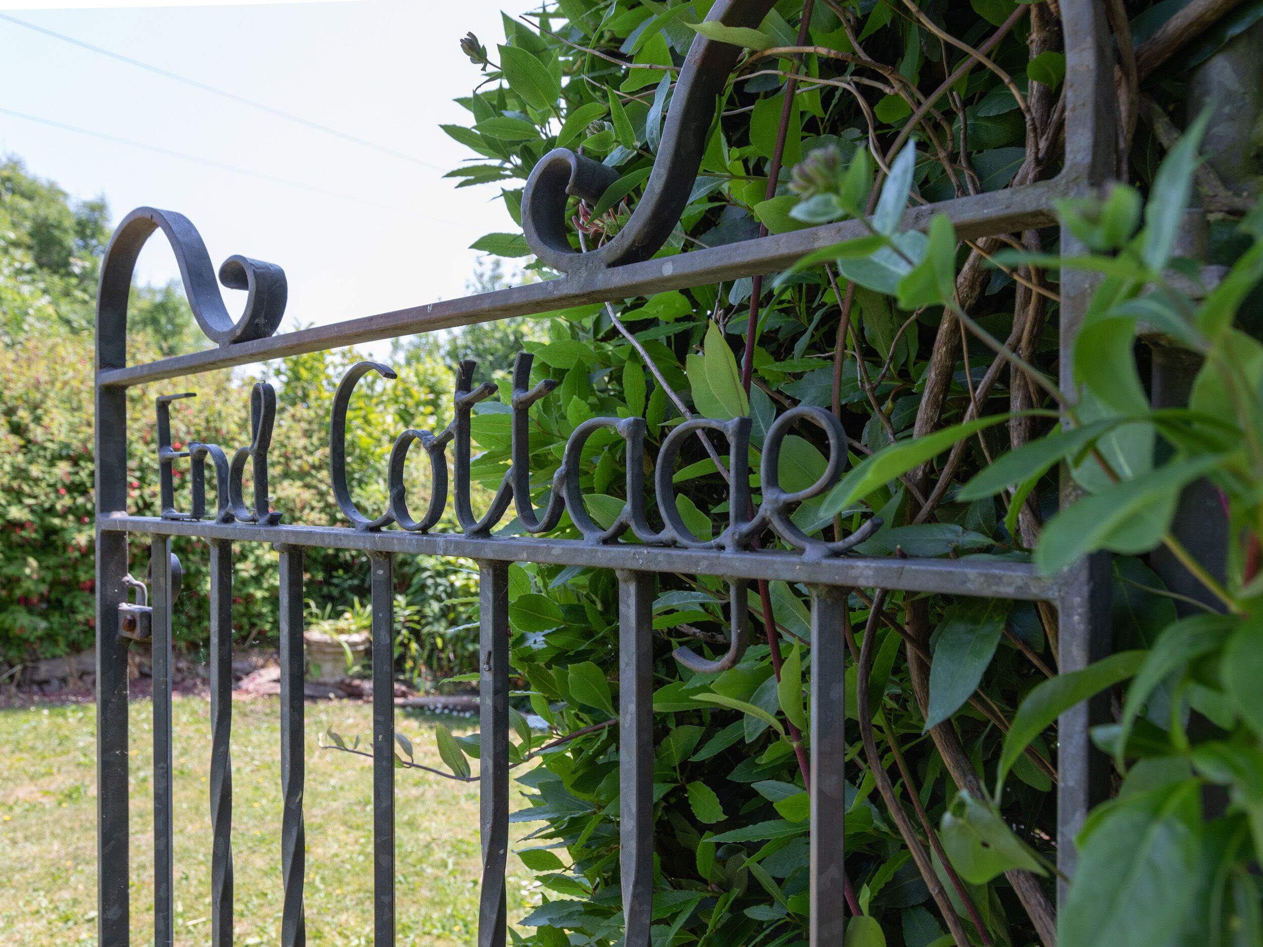 Um portão de ferro forjado com a inscrição "Find Cottage", rodeado por vegetação.