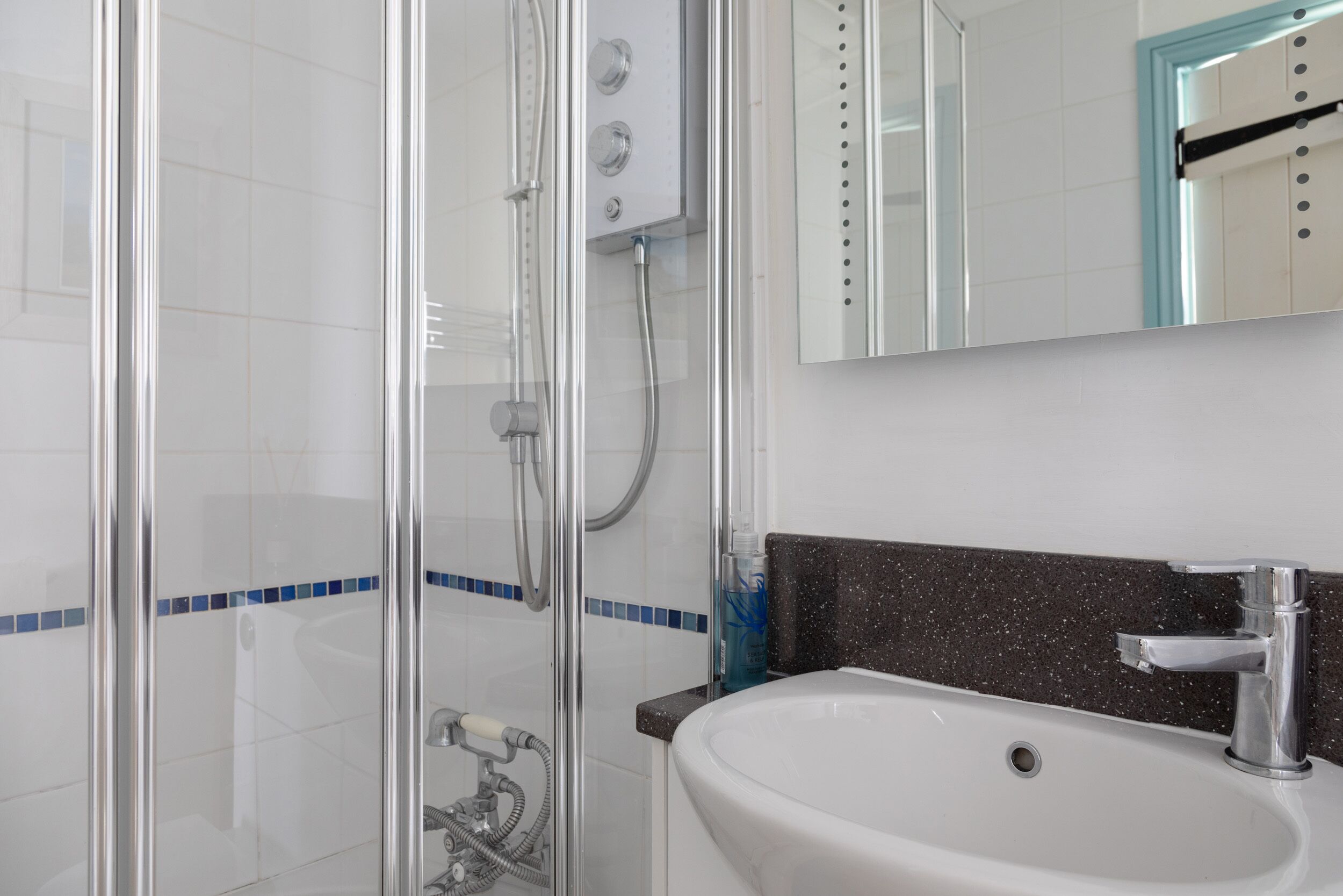 Un baño con ducha de vidrio, un lavamanos blanco con encimera negra y un espejo sobre el lavamanos.