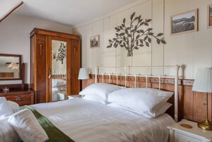 Un dormitorio ordenado con una cama grande, un armario de madera, un espejo y una planta en la pared.