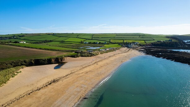 An aerial view of a coastal area with a sandy beach, green fields, and a few buildings. - End Cottage (Kingsbridge)