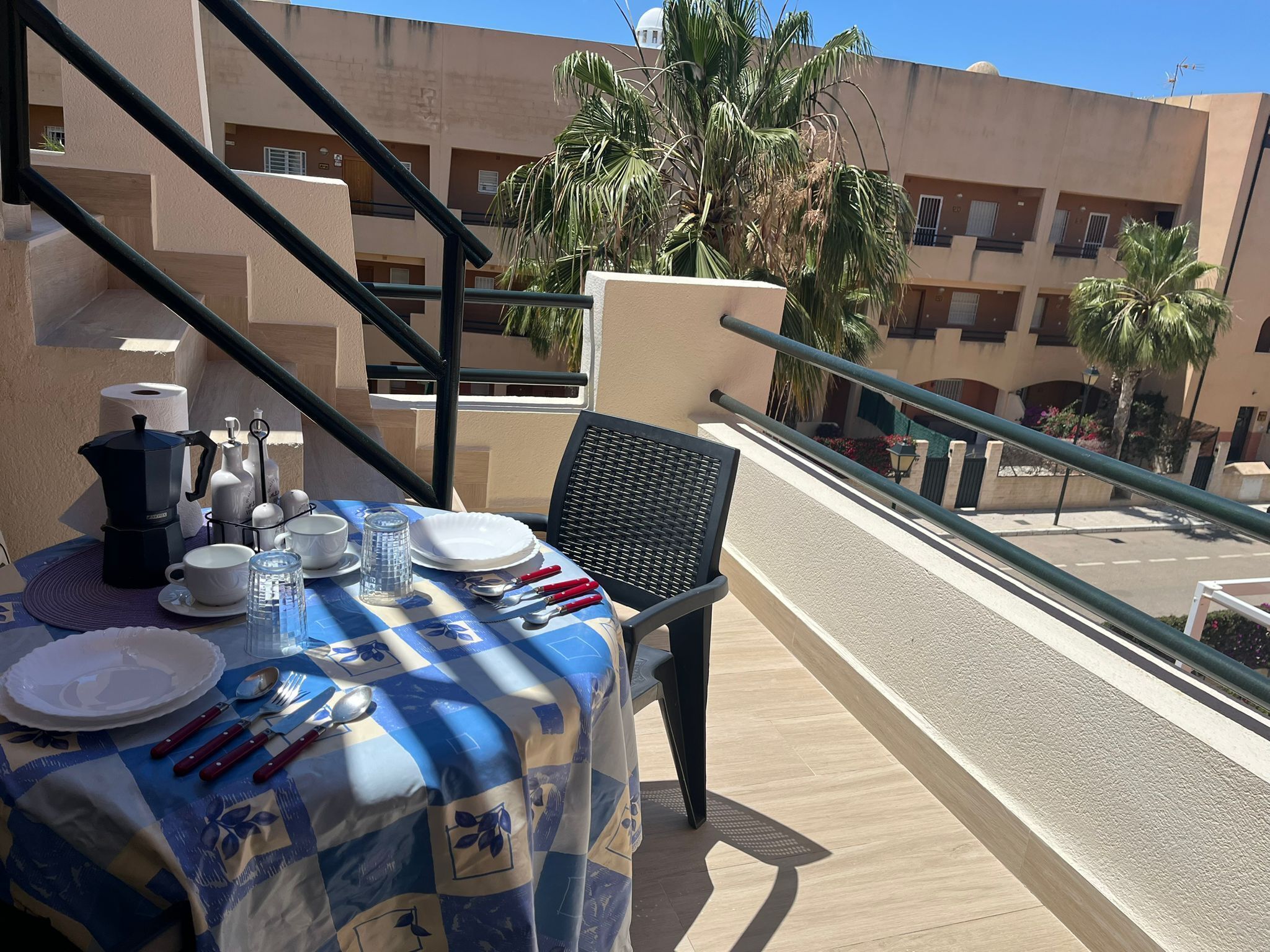 A balcony with a table set for dining, a chair, and a view of a building with palm trees.